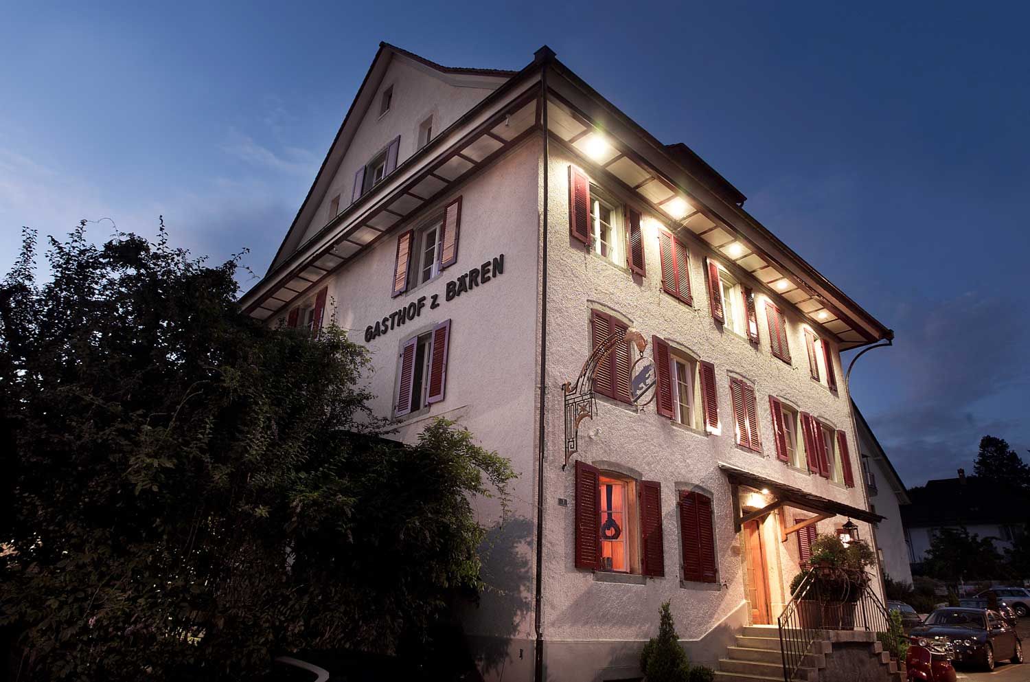 Das klassizistische Haus zur blauen Stunde, mit rotem Fensterläden und erleuchteten Fenstern
