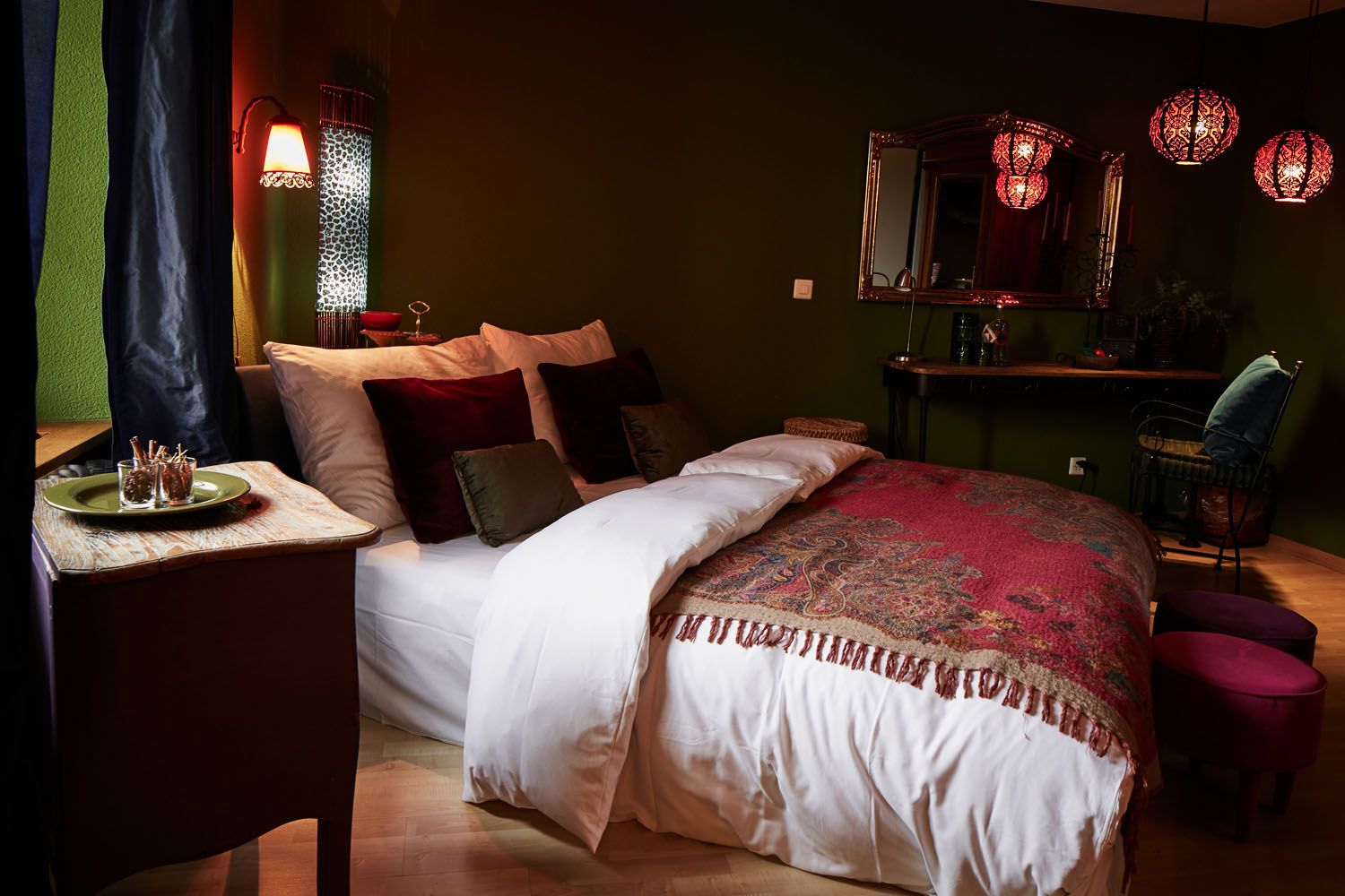 Ein Doppelzimmer mit dunklen Wänden, Laternen und bestickter Tagesdecke